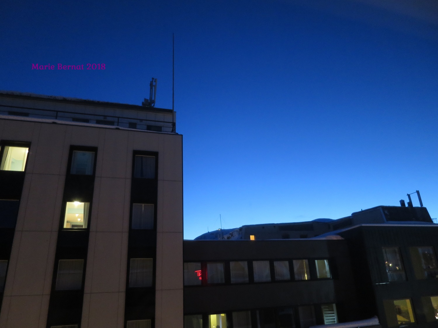 Lever de soleil à 9h - un peu de lumière apparaît à l'horizon, au dessus de la montagne et des batiments en face.